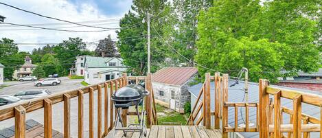 A wooden deck with a grill and a view of a street with houses and cars.
