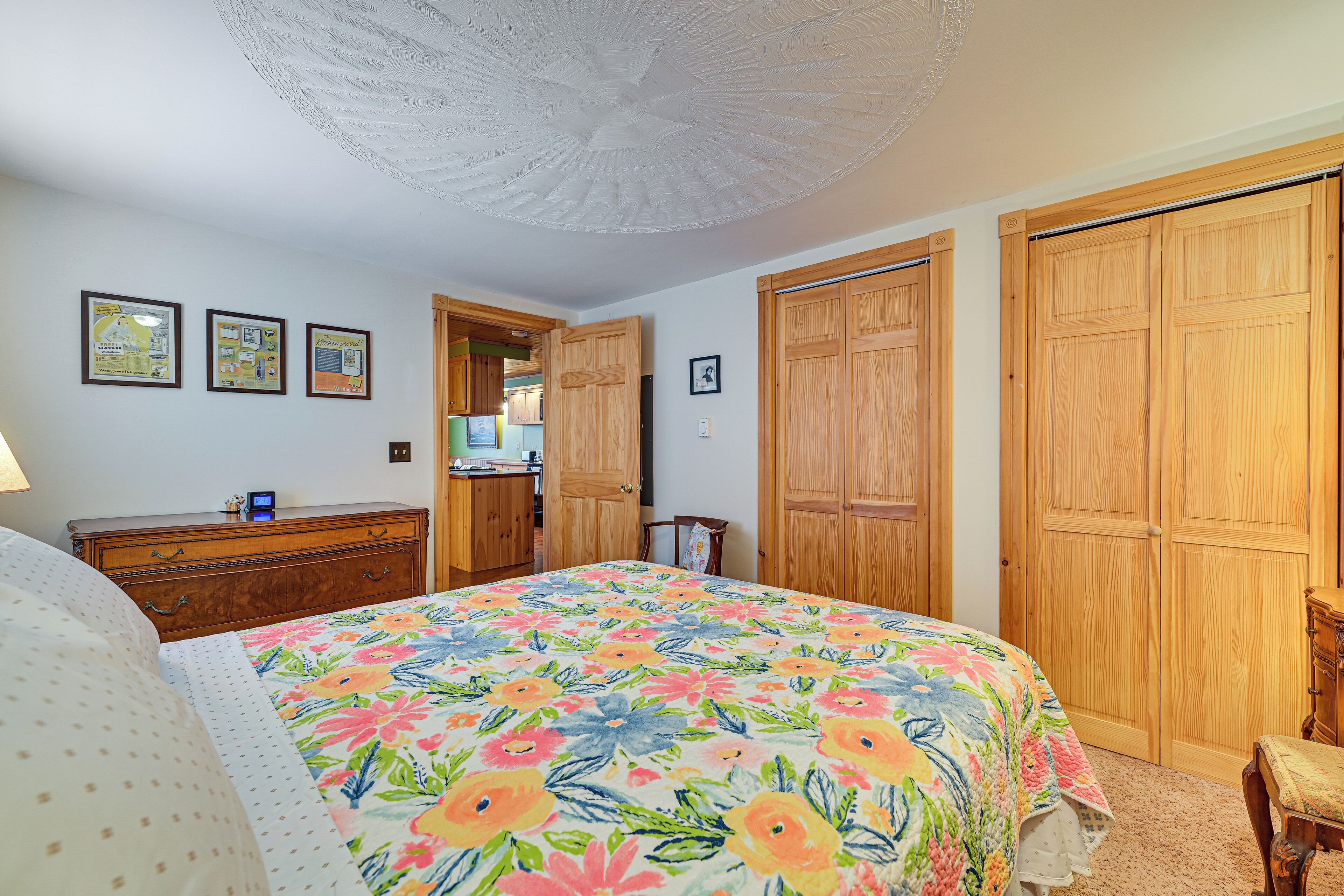 A bedroom with a floral bedspread, wooden wardrobe, and a ceiling fan.
