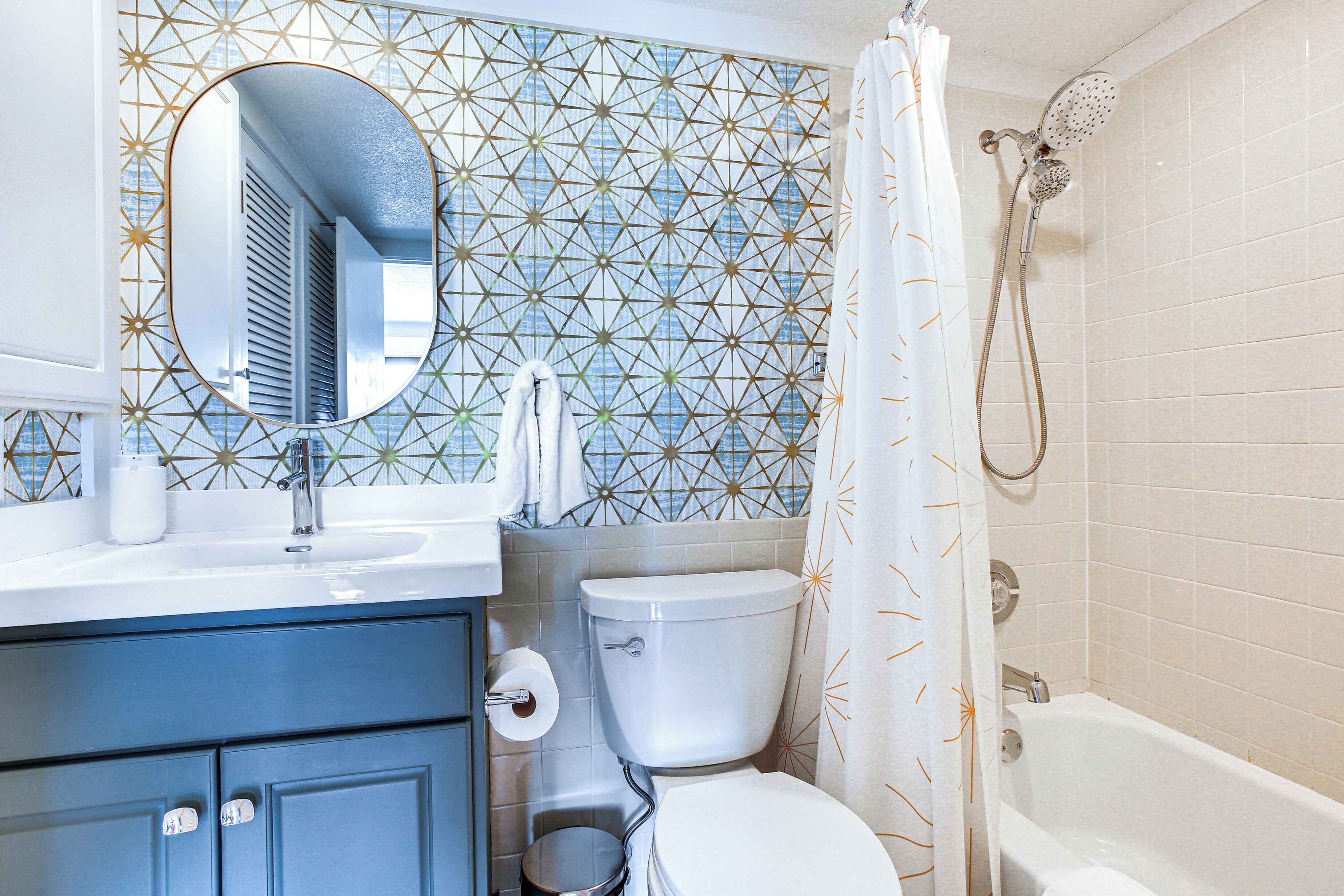 A bathroom with a geometric patterned wall, a white toilet, a sink with a mirror, and a shower.