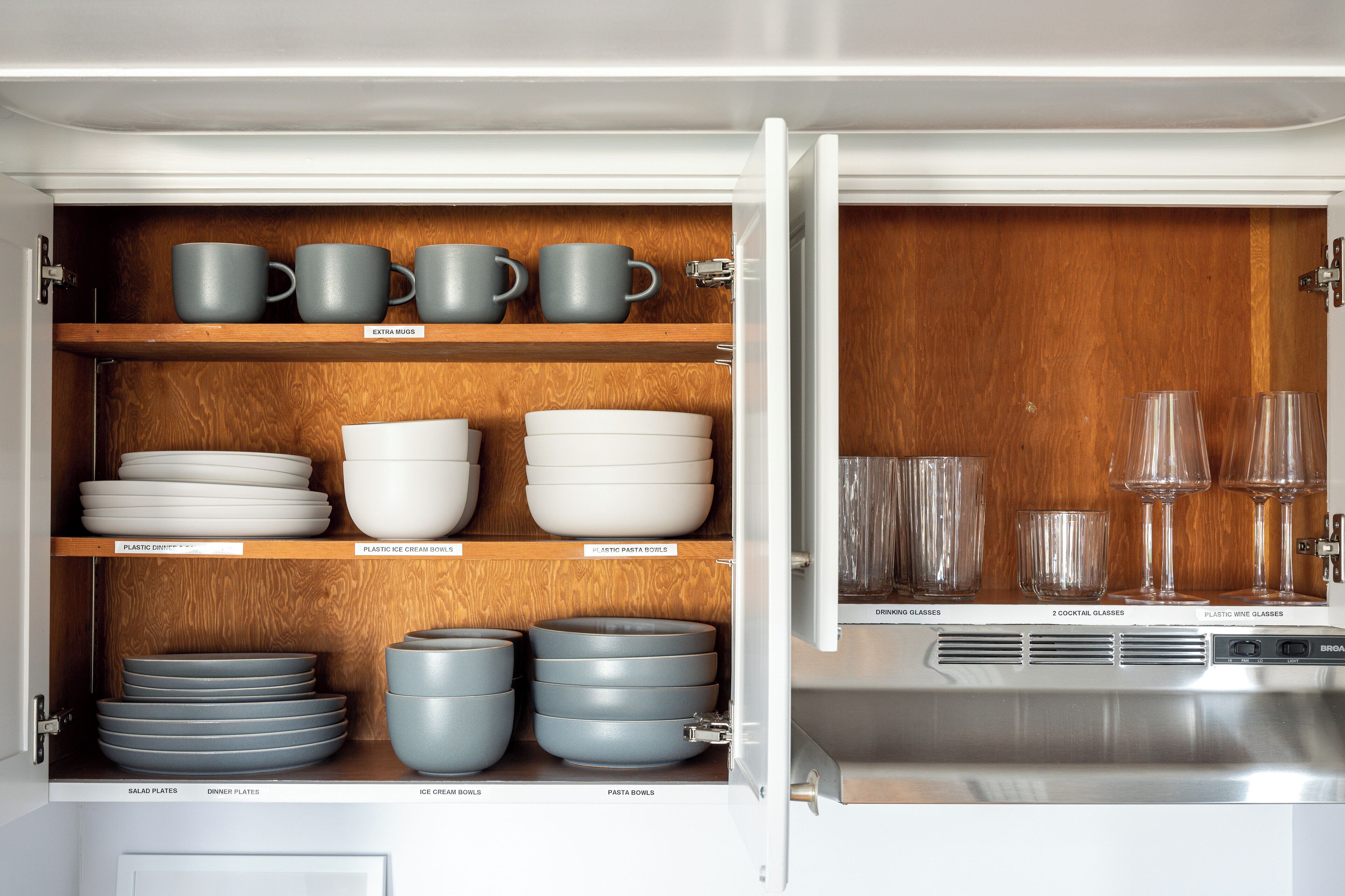A kitchen cabinet with labeled compartments for various dishes and glasses.