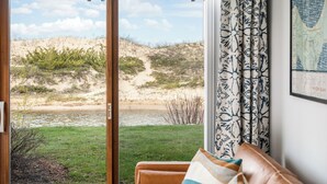 Habitación con vista a una playa y dunas a través de una puerta corrediza de vidrio.