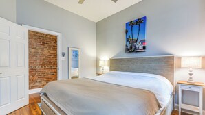 Ein Schlafzimmer mit einem großen Bett, einer Ziegelwand, Holzboden, einem Nachttisch mit Lampe und einem Gemälde an der Wand.