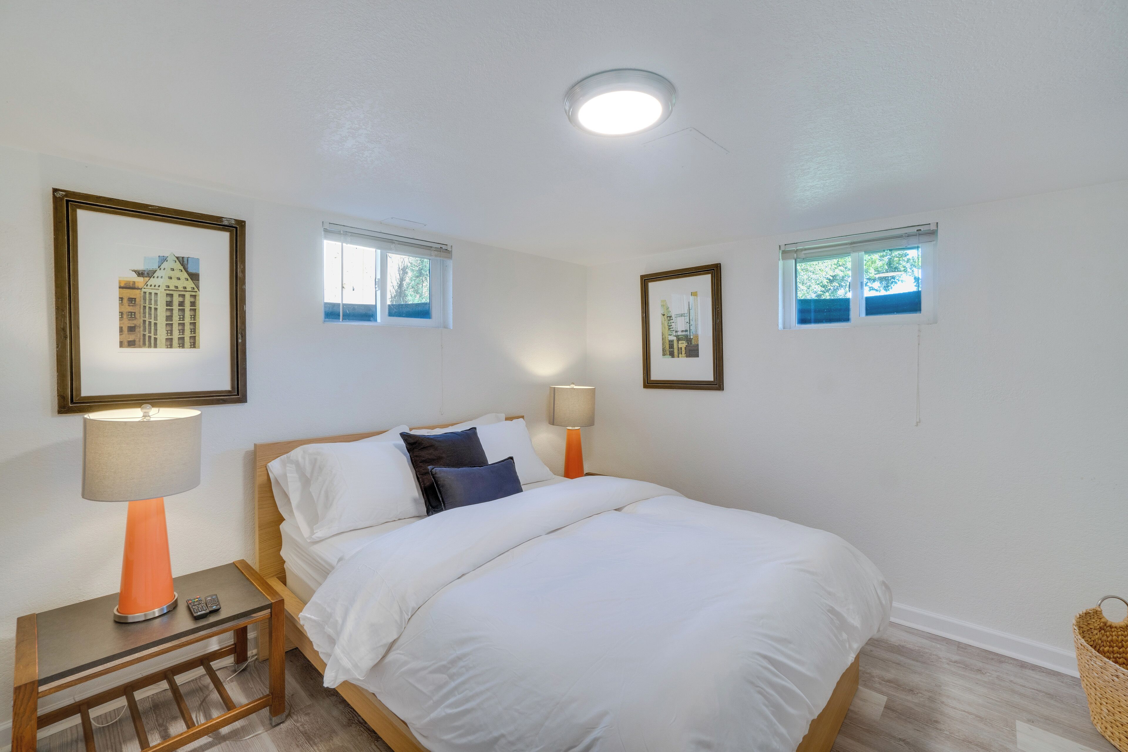 Un dormitorio con una cama, dos mesitas de noche con lámparas, cuadros en la pared y una ventana.