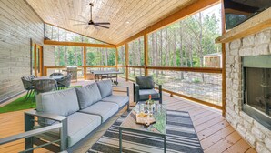 Une vaste terrasse dotée d’un plafond en bois, d’une cheminée en pierre et offrant une vue sur la forêt environnante.