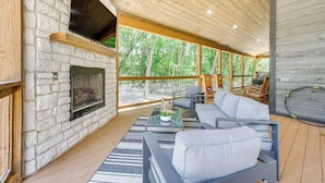 Un salon chaleureux avec une cheminée en pierre, un plafond en bois et de grandes fenêtres donnant sur une forêt.