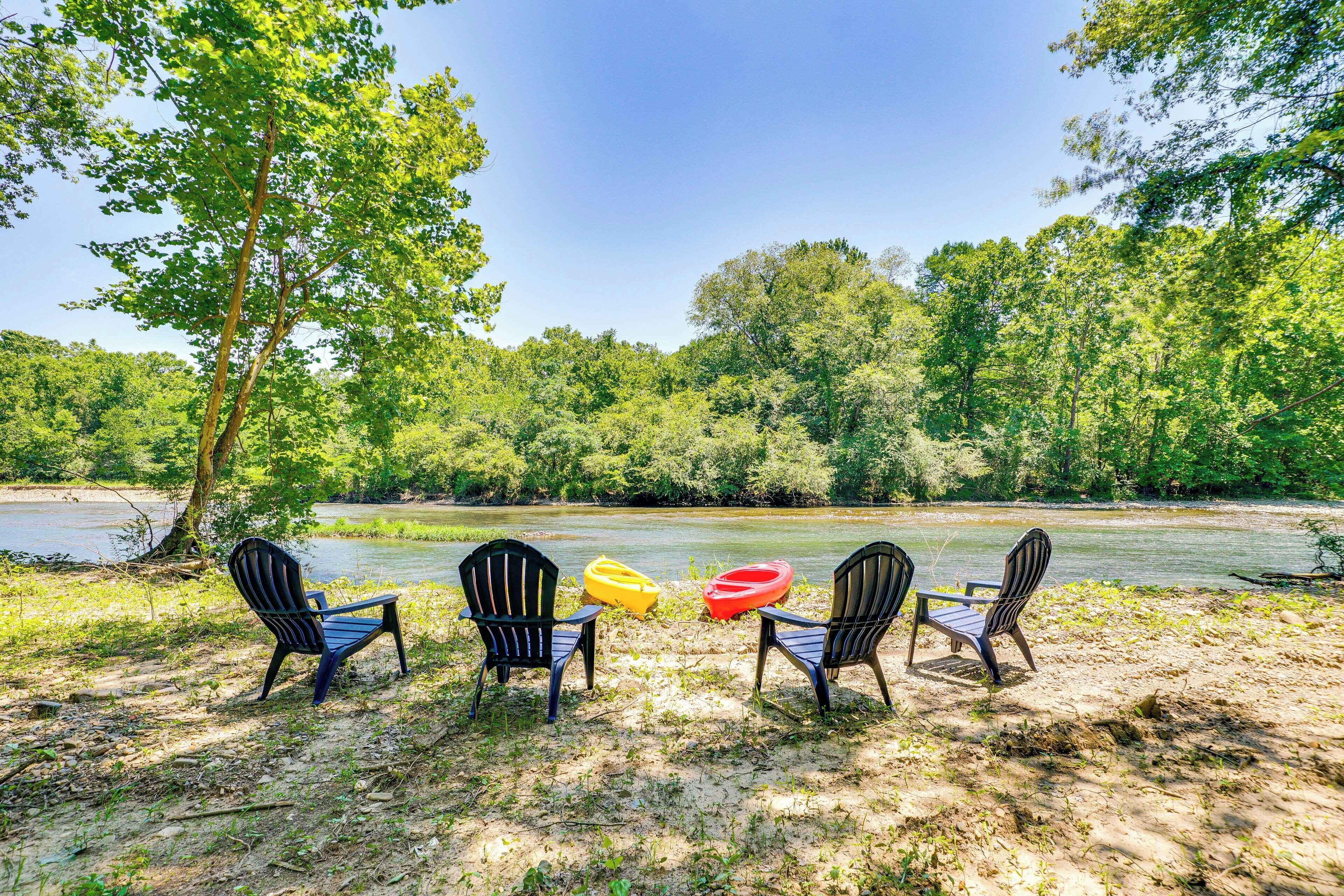 A riverside seating area with four chairs and two kayaks.