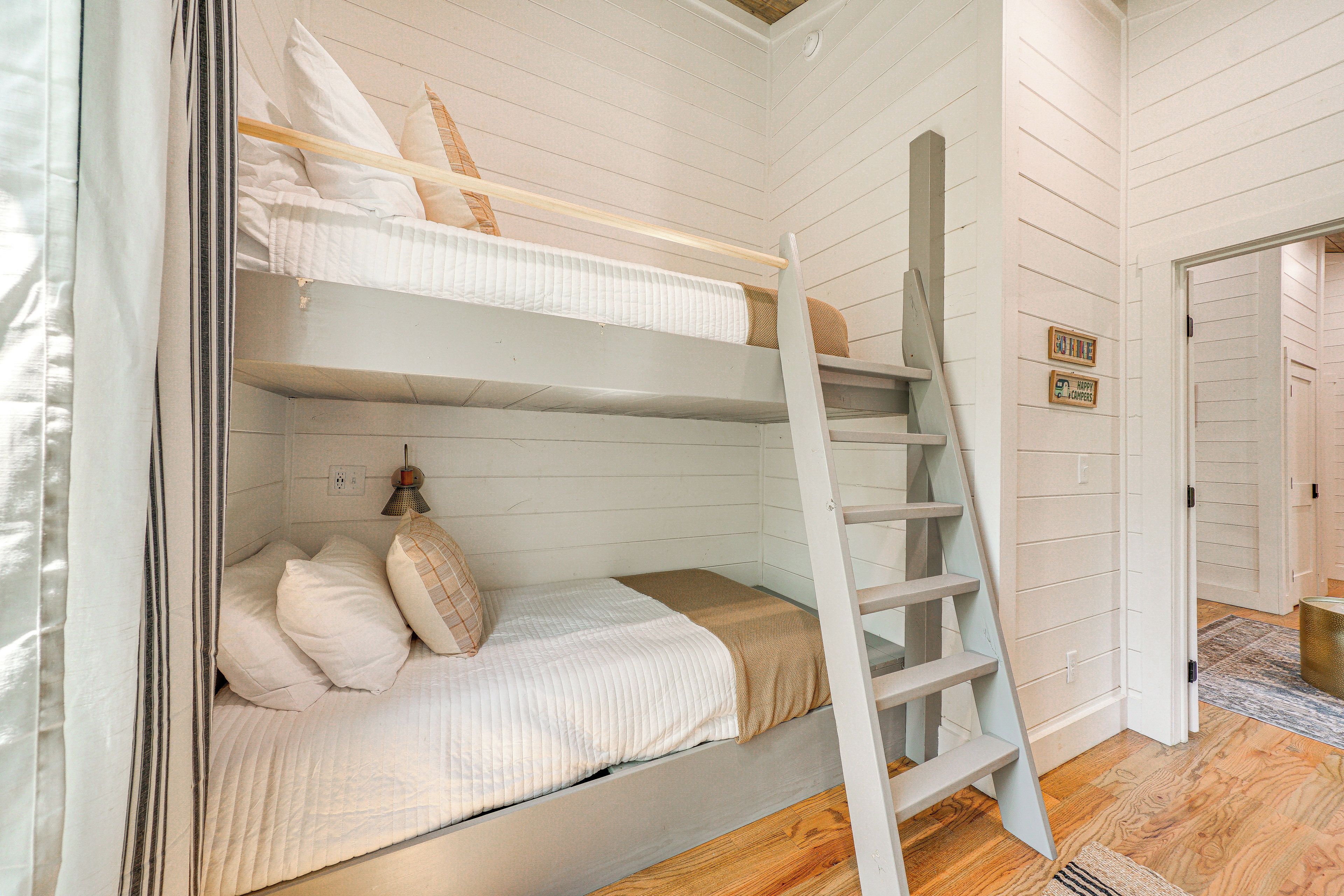 Un lit superposé avec une échelle, des murs blancs et un plancher en bois.