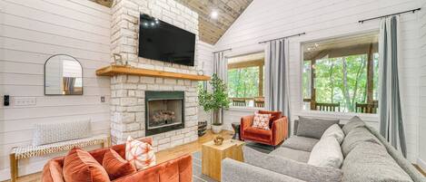 A cozy living room with a stone fireplace, a large flat-screen TV, and a comfortable seating area with a sofa and armchairs.