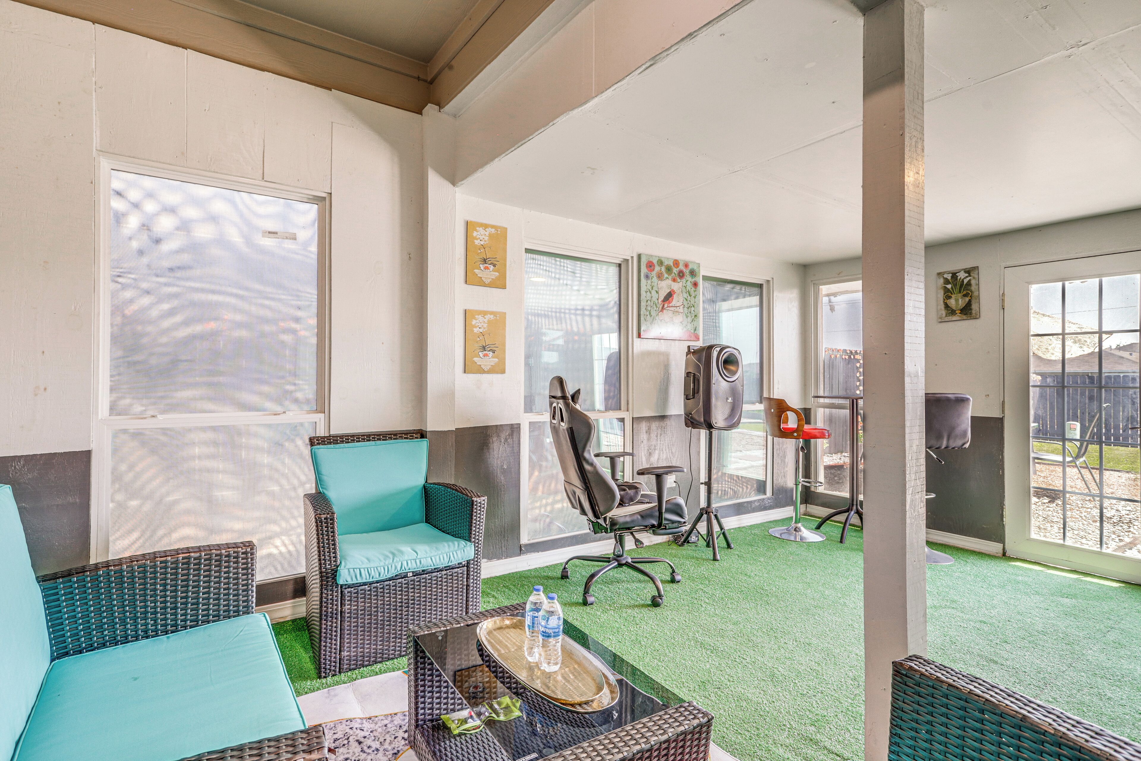 A room with wicker furniture, a glass coffee table, and a green artificial turf floor.