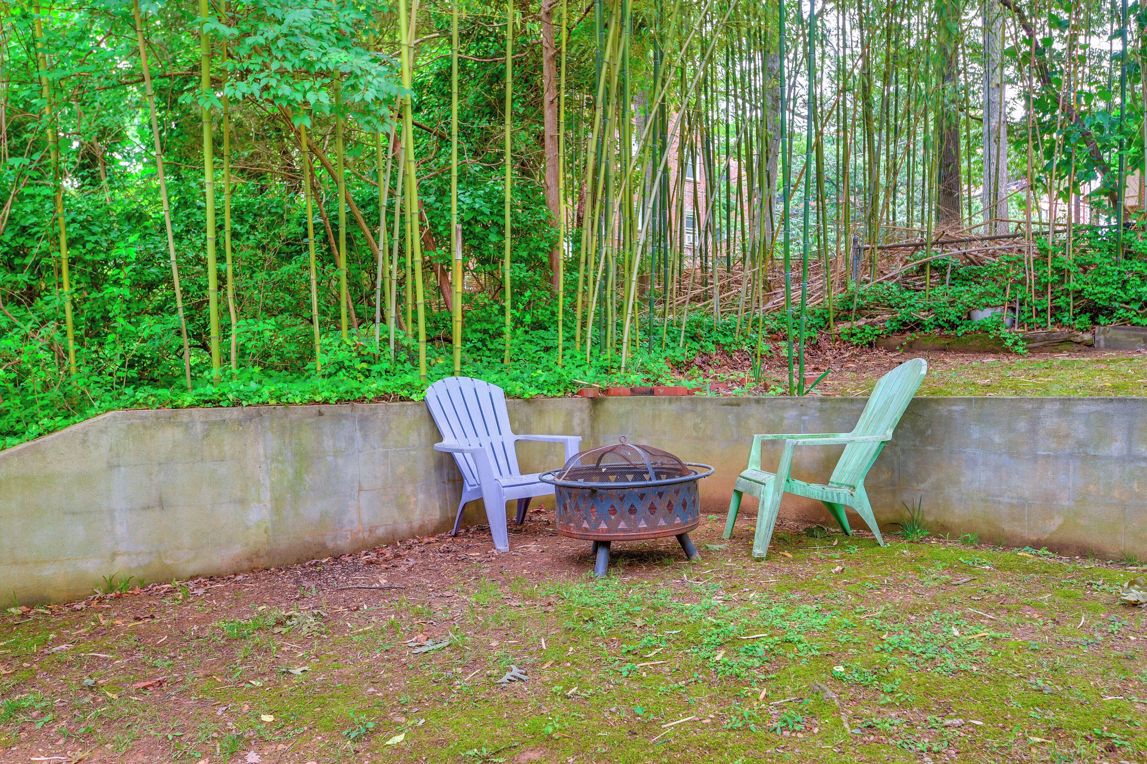 Deux chaises et un foyer extérieur dans un jardin, avec un mur en béton et des bambous en arrière-plan.