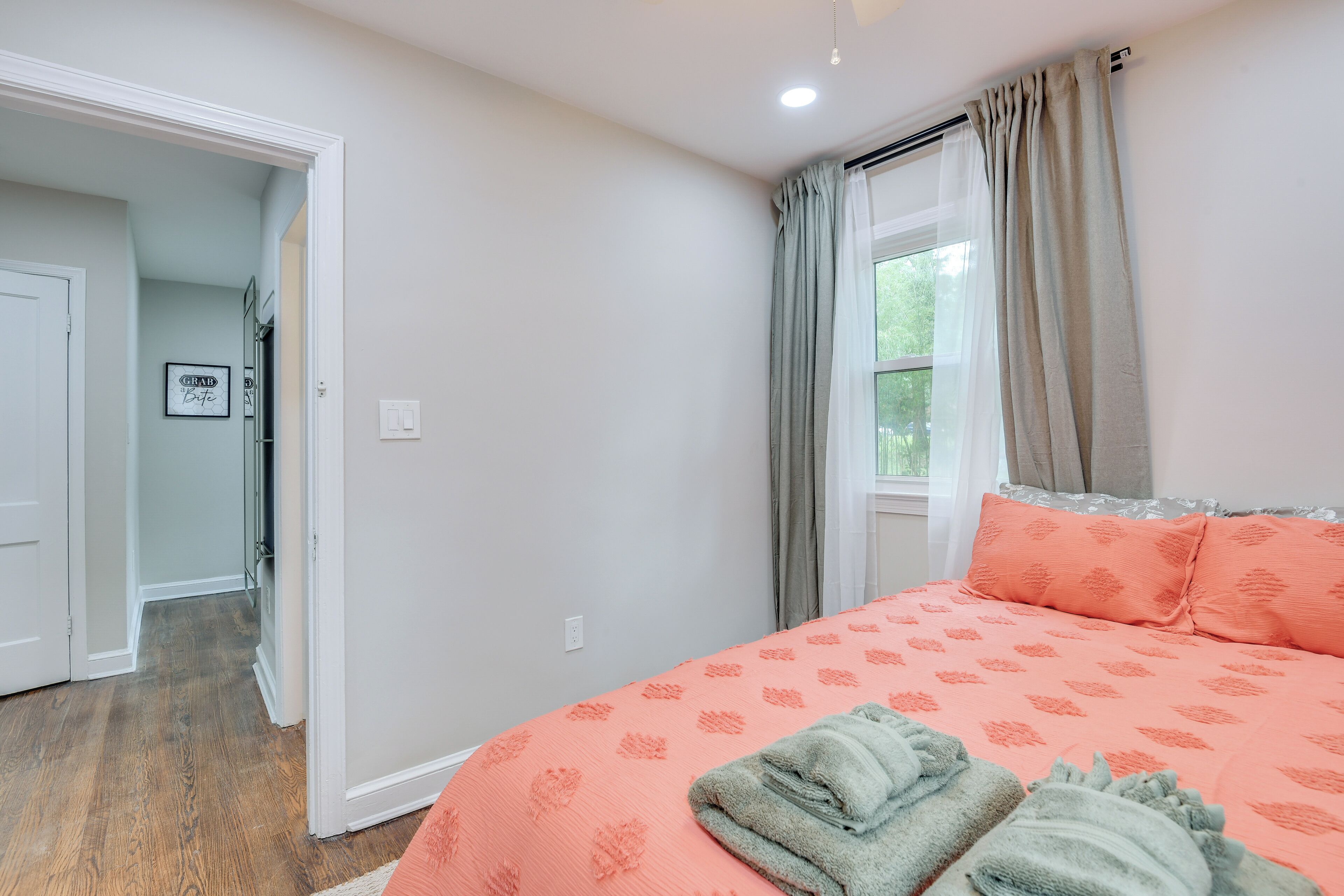 Une chambre à coucher avec un lit, une fenêtre avec des rideaux, une porte et un couloir.