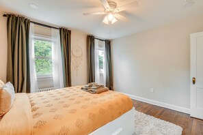 Une chambre à coucher avec un lit, un ventilateur de plafond et une fenêtre avec des rideaux.