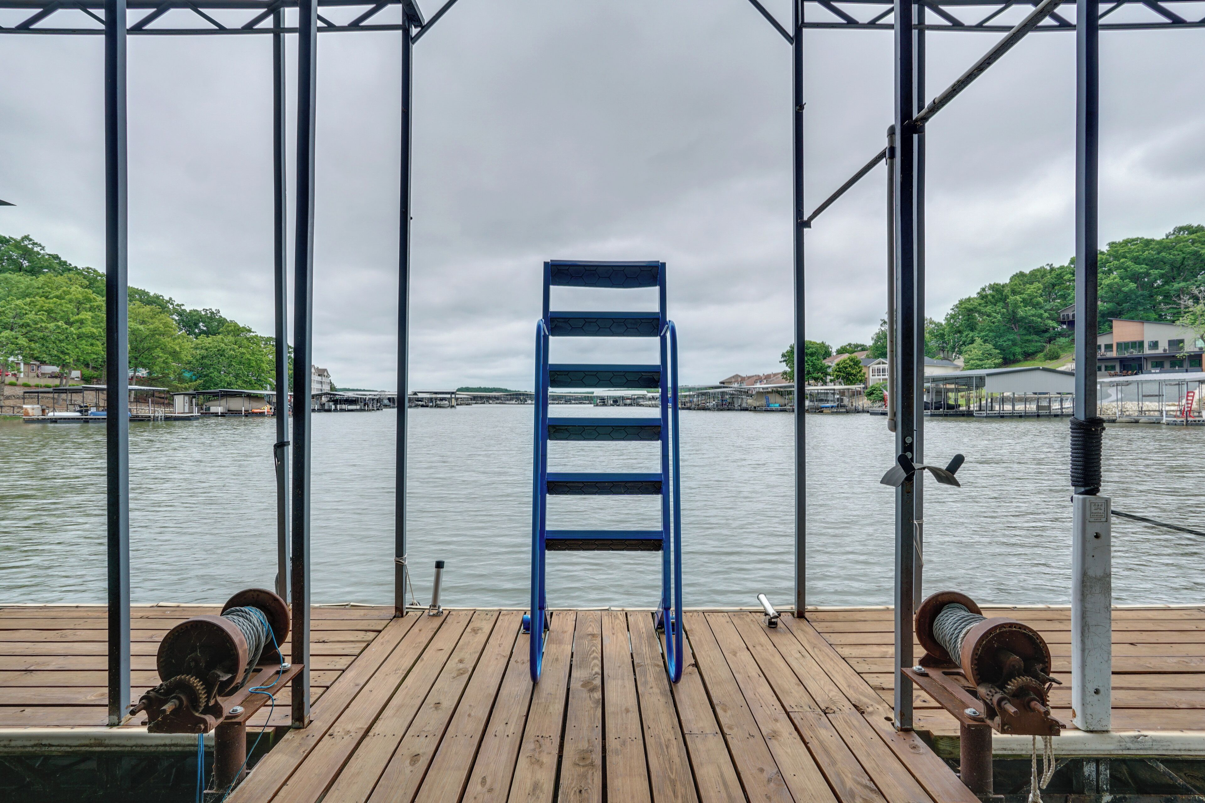 A wooden dock with a blue metal ladder, a winch, and a metal railing.
