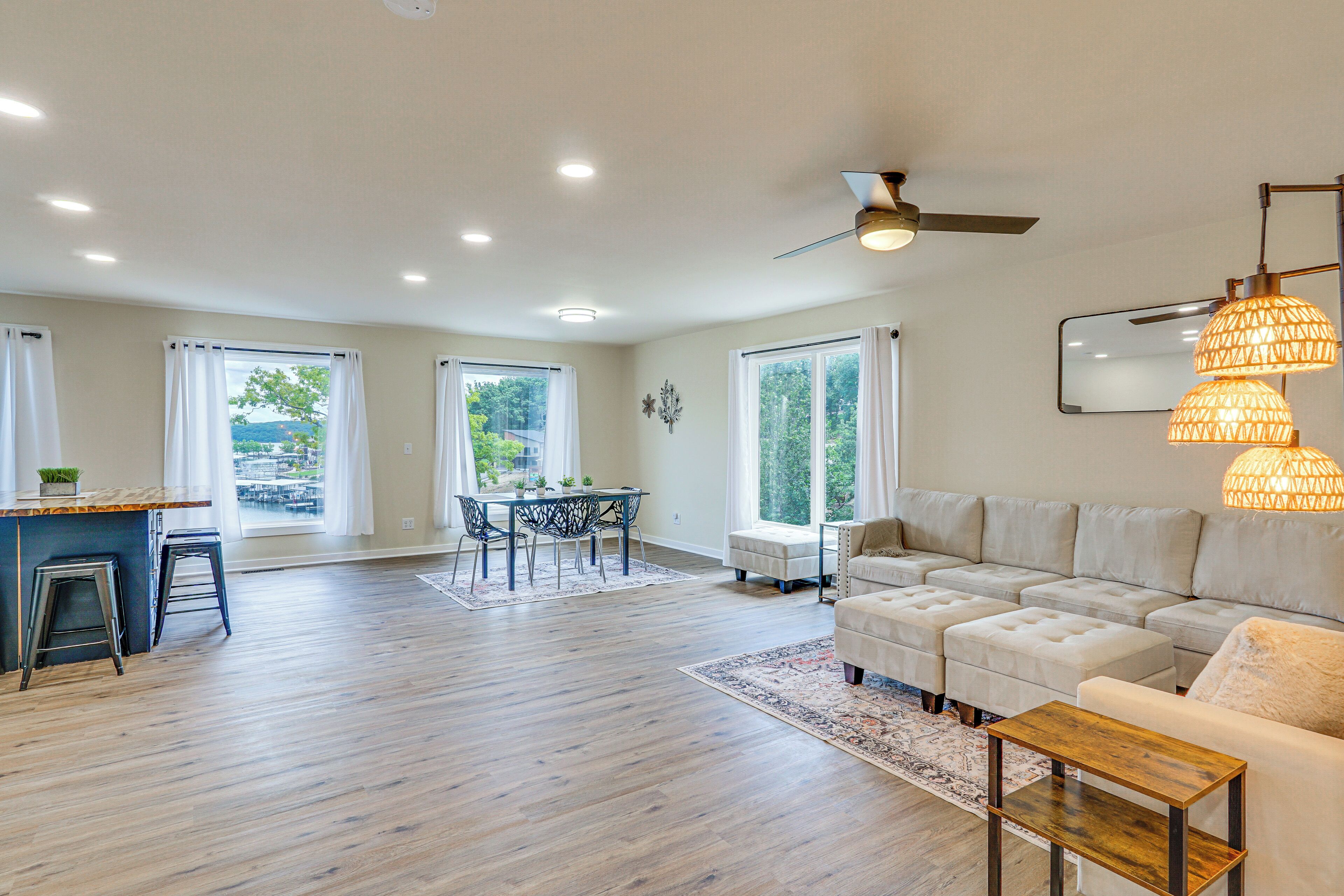 A spacious living room with a sofa, ottoman, and a coffee table. There is a dining area with a table and chairs, and a kitchen area with a bar and stools.