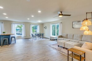 A spacious living room with a sofa, ottoman, and a coffee table. There is a dining area with a table and chairs, and a kitchen area with a bar and stools. - Kayaks, Boat Slip, Game Room, Calm Cove, Great Loc (Osage Beach)