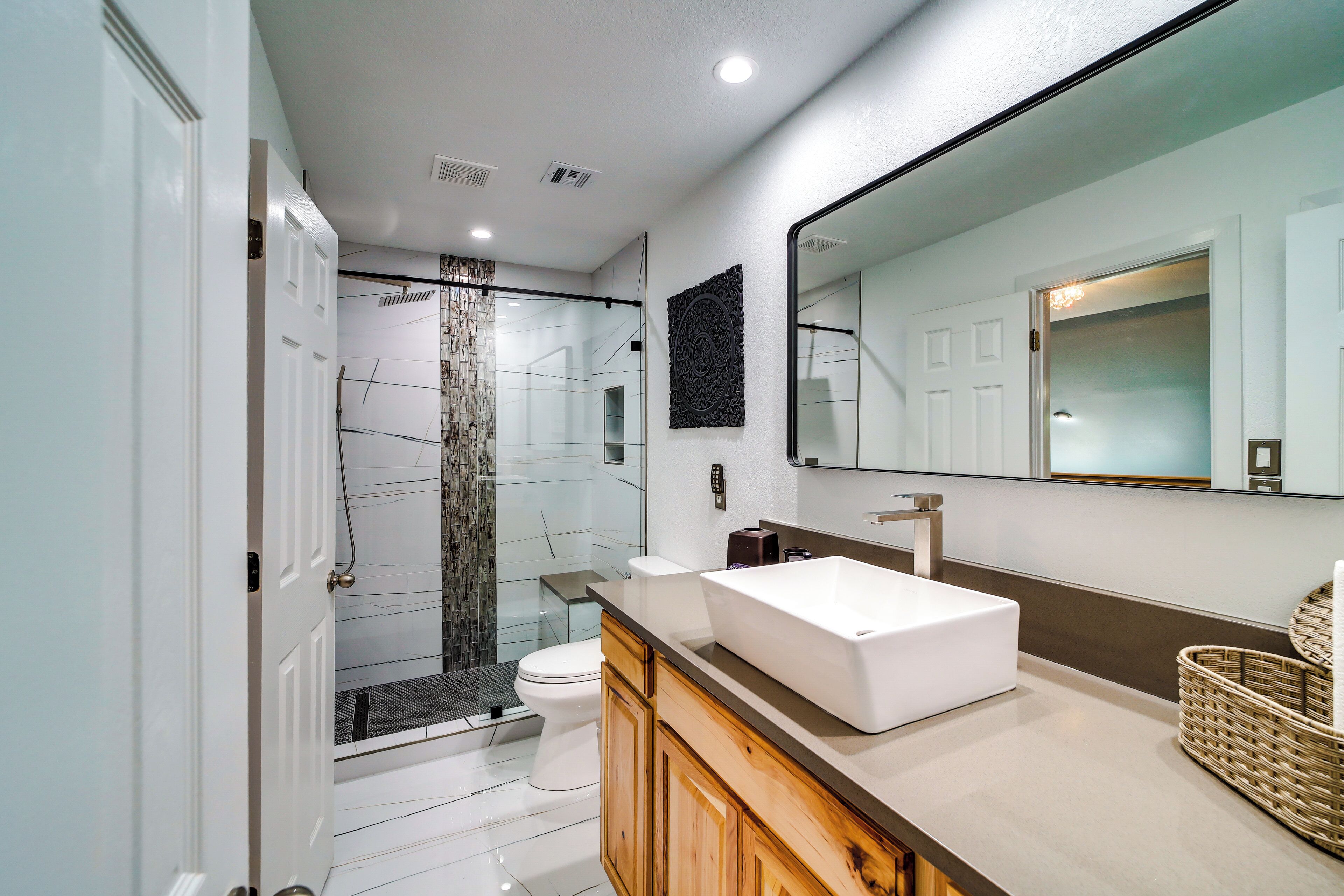 A modern bathroom with a large mirror, a white sink, and a shower area.
