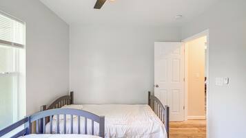 A bedroom with two single beds, a ceiling fan, a white door, and a window with blinds.