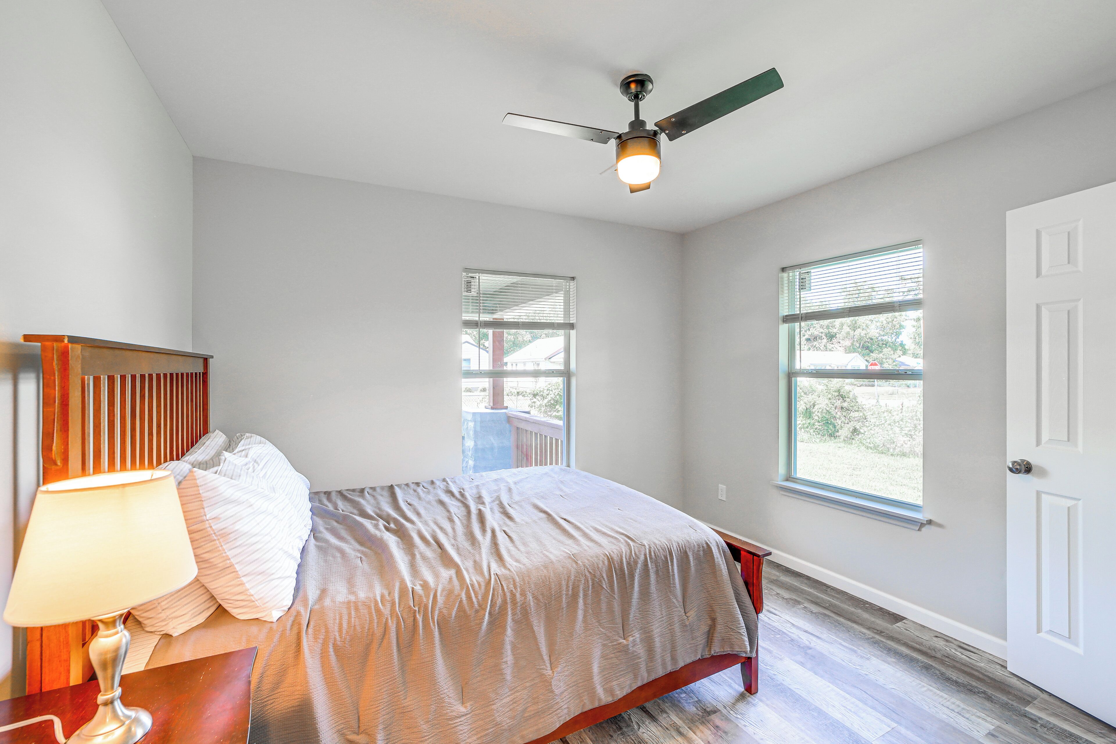 A bedroom with a bed, a nightstand, a lamp, a ceiling fan, and two windows.