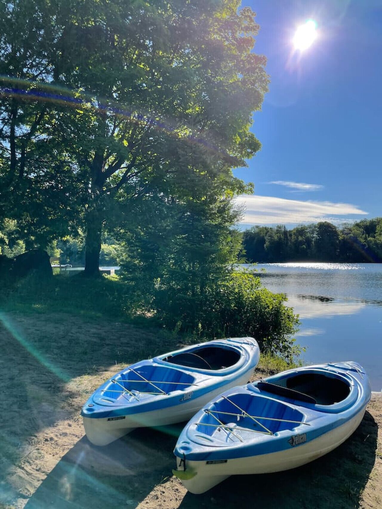 Deux kayaks sont garés au bord d’un lac, avec des arbres et un ciel dégagé en arrière-plan.