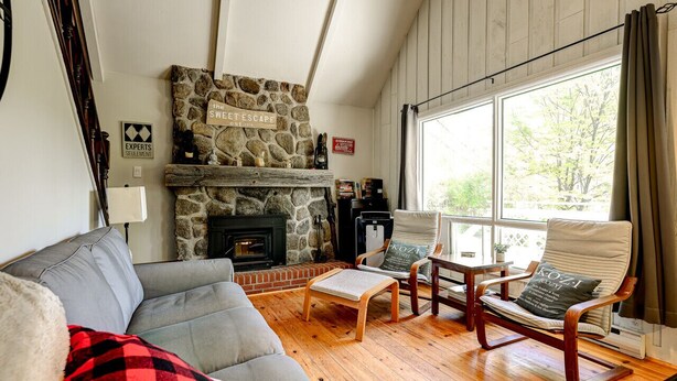 Ein gemütliches Wohnzimmer mit Kamin aus Stein, Holzboden und einem großen Fenster mit Vorhängen.