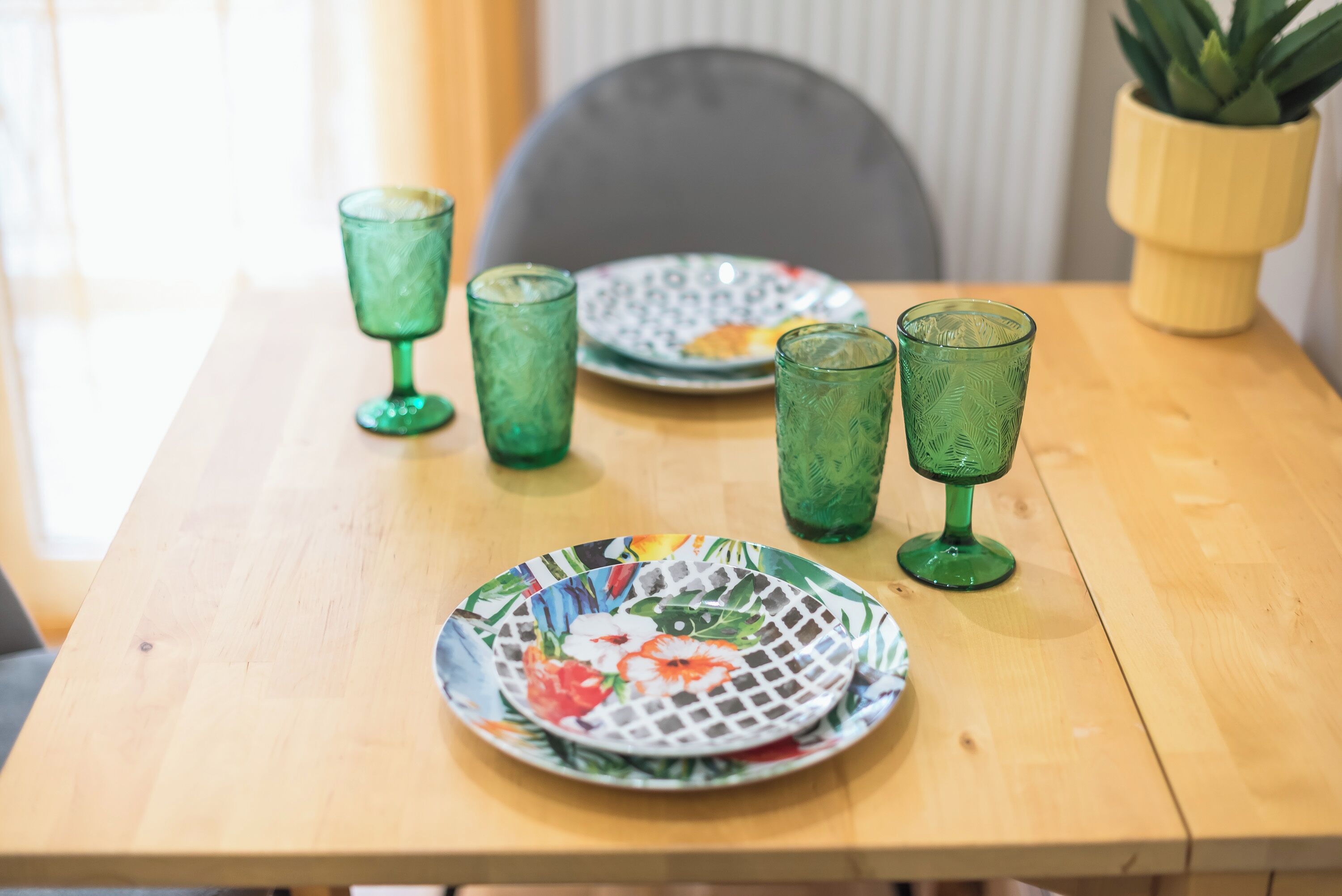 A wooden table with a floral plate and three green glasses.