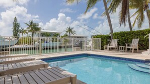 A pool area with lounge chairs, a fenced deck, and palm trees. - Large home with a private pool! (Key Colony Beach)