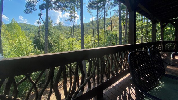 A wooden deck with a railing, overlooking a forested area with tall trees and a clear sky. - Peaceful and secluded with year-round mountain views and waterfall sounds. (Cherry Log)