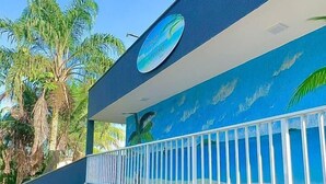 A building with a blue exterior, a balcony with a white railing, and a sign with palm trees. - POUSADA BRISA MAR UBATUBA (Ubatuba)