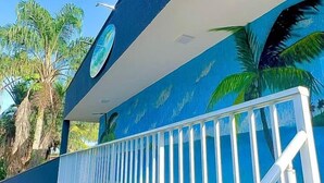 A building with a blue exterior, a white railing, and a mural of palm trees. - POUSADA BRISA MAR UBATUBA (Ubatuba)