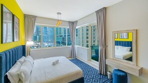 A hotel room with a large bed, a city view, a window with curtains, and a mirror with a yellow frame. - Modern 2BR with full Sea View | Pool & Gym (Dubai Marina)