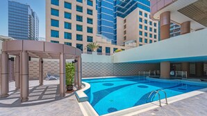 A swimming pool with a sunken center, surrounded by a covered area with lounge chairs, set against a backdrop of modern buildings. - Modern 2BR with full Sea View | Pool & Gym (Dubai Marina)
