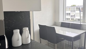 A modern kitchen with a marble countertop, white cabinets, and a dining area with a table and chairs. - Cozy Viby Apartment Near Kjaerlsund (Aarhus)