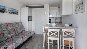 Eine kompakte Küche mit weißen Schränken, ein Essbereich mit weißen Stühlen und ein Sofa mit London-Motiv.