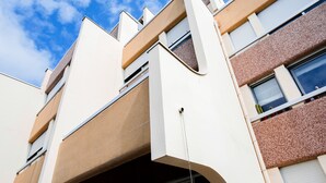 Un edificio moderno con un diseño arquitectónico singular, que presenta una combinación de fachadas blancas y marrones, ventanas amplias y un balcón visible.