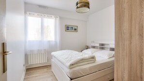 Un dormitorio con cama, mesita de noche, lámpara, un cuadro en la pared y ventana con cortinas.