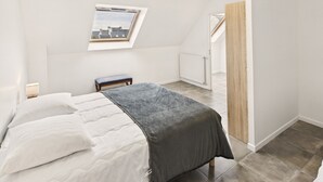 A bedroom with a bed, a bench, a skylight, and a view of the outside.
