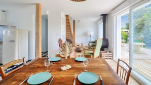 Comedor con una mesa de madera dispuesta para cuatro, una cocina al fondo y vistas al exterior a través de amplios ventanales.