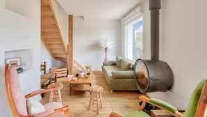 Una sala moderna con una escalera de madera, un sofá verde, una mesa de comedor de madera y una chimenea negra grande.
