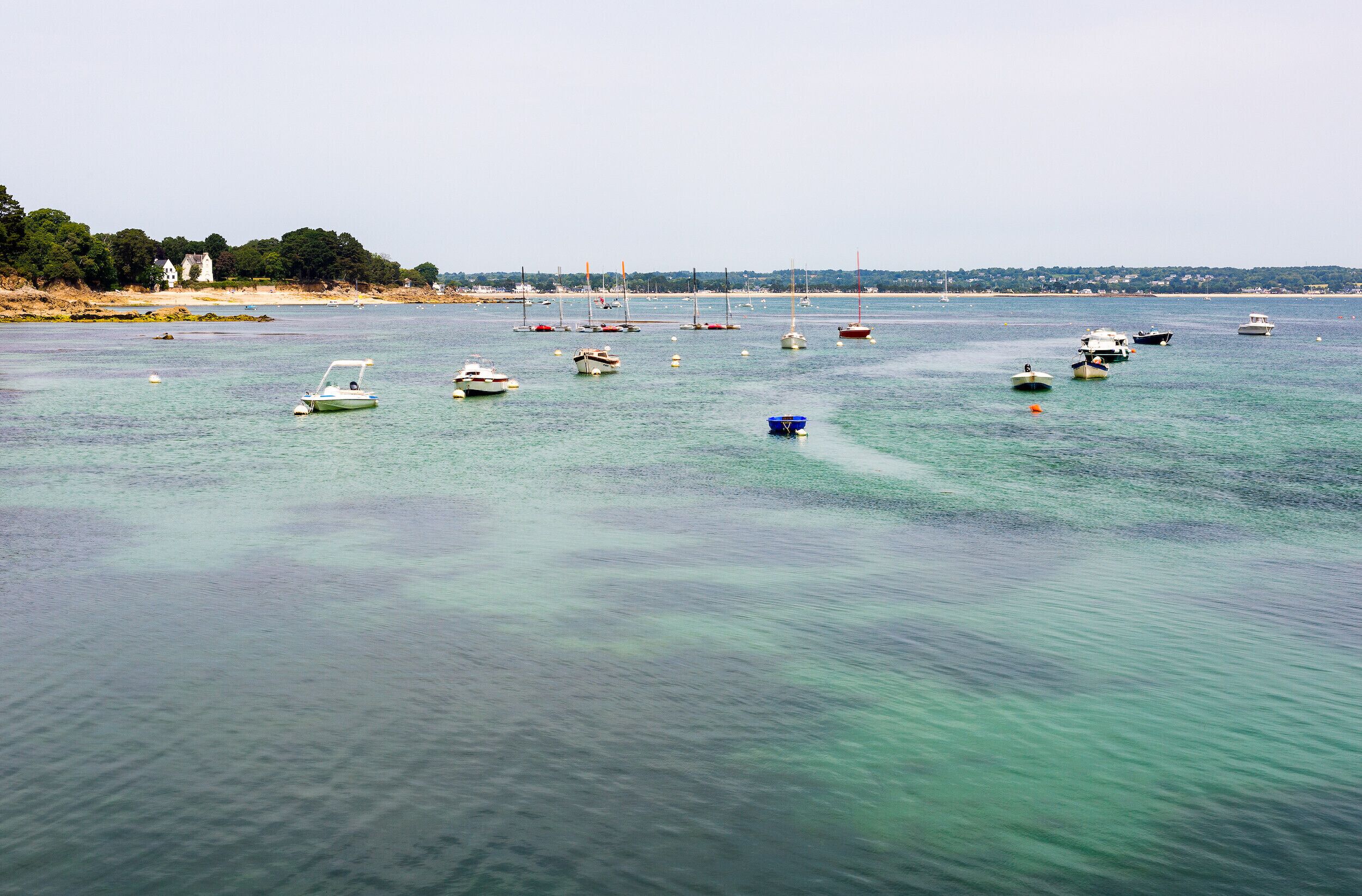 A marina with various boats anchored in calm waters, surrounded by a coastal landscape.