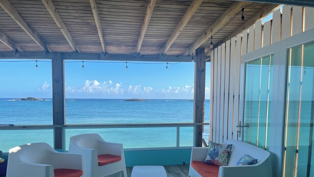 A covered outdoor seating area with wicker furniture and a view of the ocean. - Mamita’s Beach House PR

 (Vega Baja)