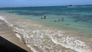 A beach with clear water, people swimming, and a lifeguard on a surfboard. - Mamita’s Beach House PR

 (Vega Baja)