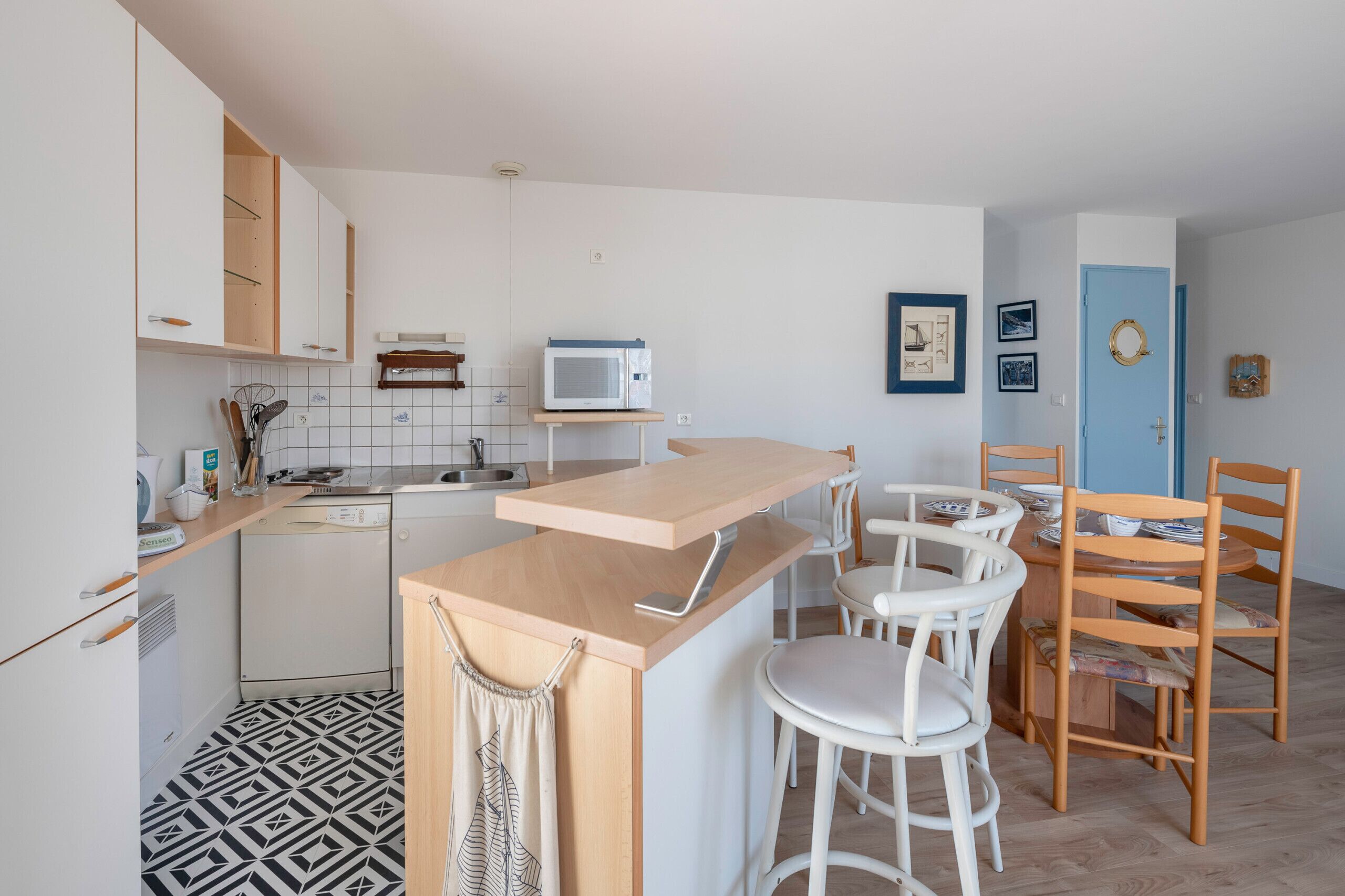 Une cuisine moderne avec des meubles blancs, un four à micro-ondes et un comptoir en bois. On y trouve des tabourets de bar blancs et des chaises en bois.