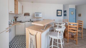 A modern kitchen with white cabinets, a microwave, and a wooden counter. There are white bar stools and wooden chairs. - On the Quai de Pornic, Apartment for 4 (Pornic)