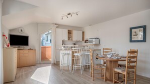 A modern kitchen with white cabinets, a microwave, and a dining area with wooden chairs and a table. - On the Quai de Pornic, Apartment for 4 (Pornic)