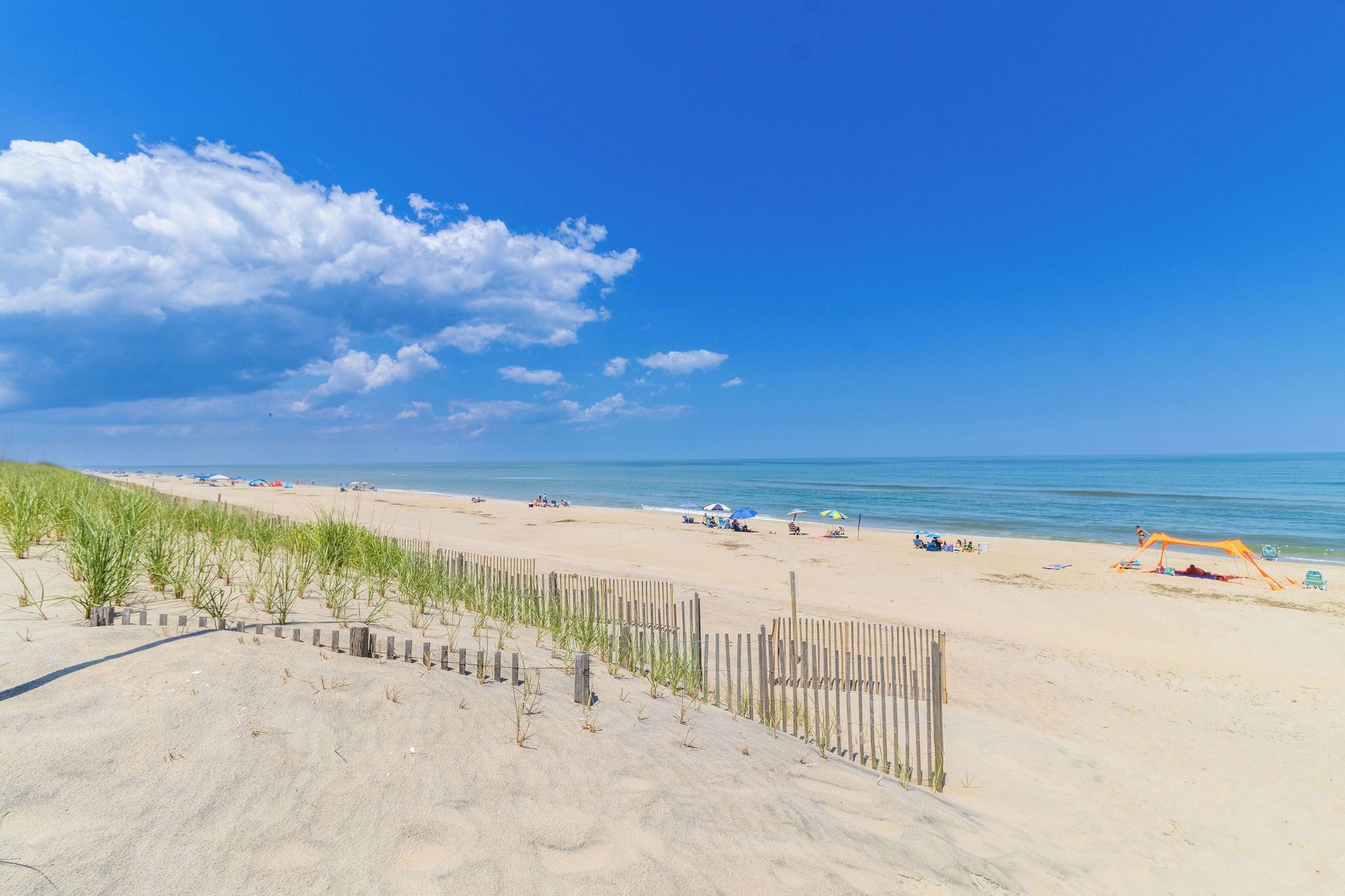 Een zandstrand met een houten omheining, strandparasols en een helderblauwe lucht.