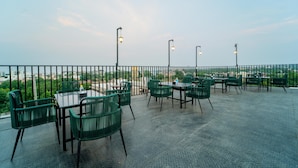 An outdoor terrace with green chairs and tables, street lamps, and a view of the cityscape. - Treebo Blu Vvu (Jodhpur)