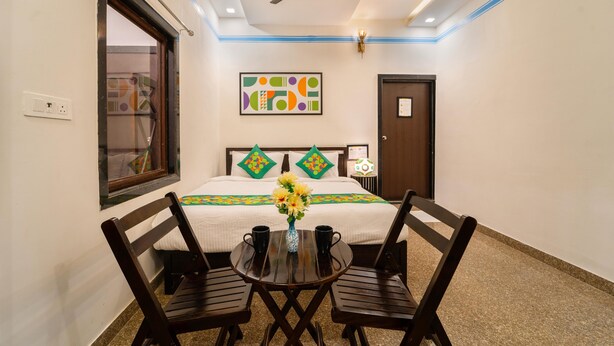 A hotel room with a bed, a ceiling fan, a window, a wall-mounted artwork, and a table with two chairs and a vase of flowers. - Treebo Blu Vvu (Jodhpur)