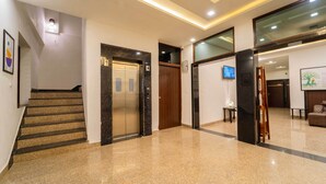 A modern lobby with a marble staircase, elevators, and a flat-screen TV mounted on the wall. - Treebo Blu Vvu (Jodhpur)