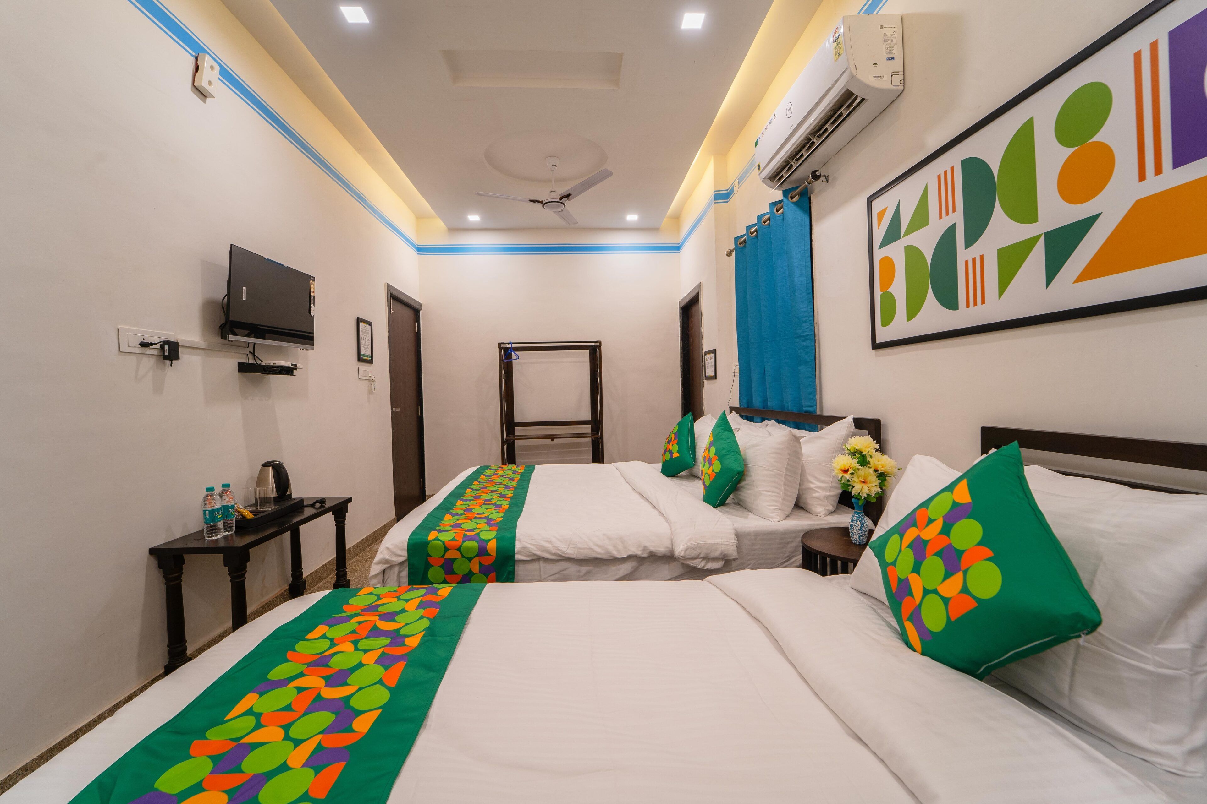 Habitación de hotel con dos camas, televisor, escritorio y ventilador de techo.