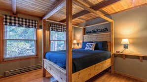 Una cama con dosel con cubrecolcha a cuadros, vigas de madera y una lámpara fijada a la pared.